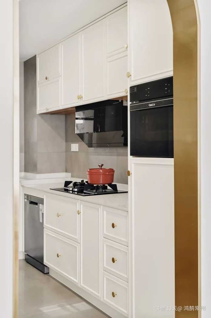 廚房呈半開放的狀態，L型櫥櫃結合拱門邊的高櫃，用於儲物和嵌入廚電，櫃門和拉手與整屋的櫃體形成統一